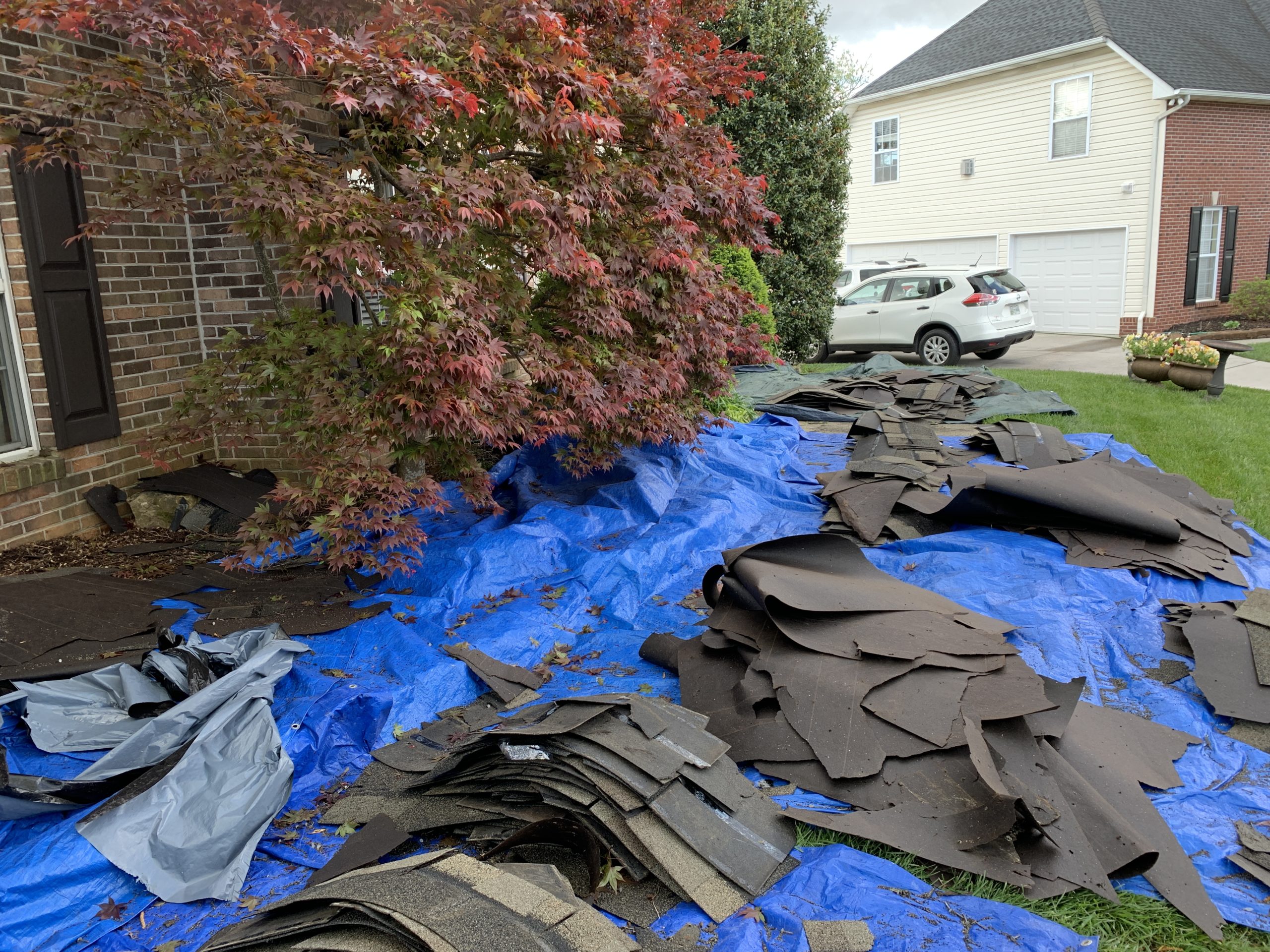 This is a view of blue tarps on the ground with old shingles that have been removed from the roof. 