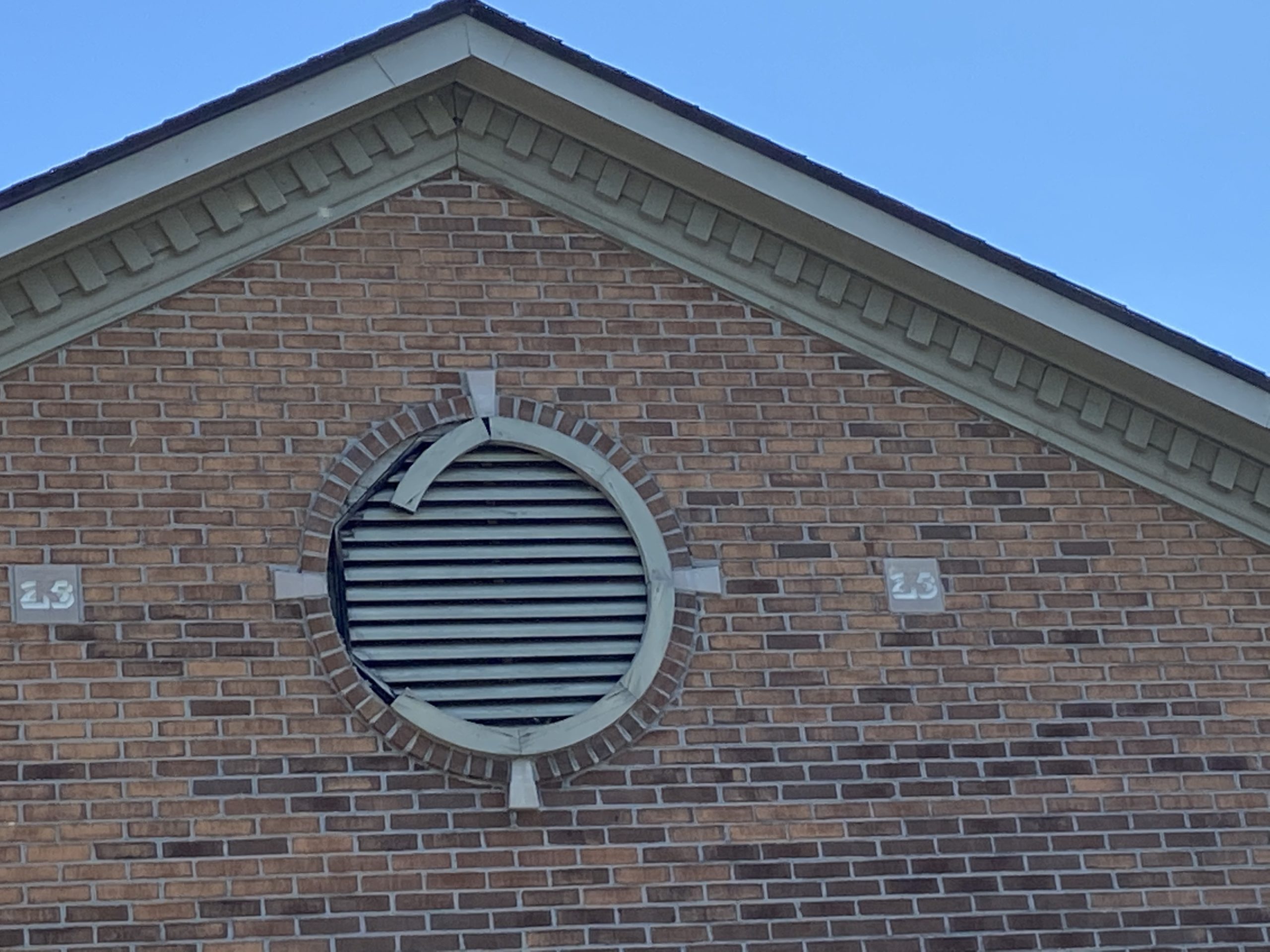 This is a view of a circular gray vent around brick. 
