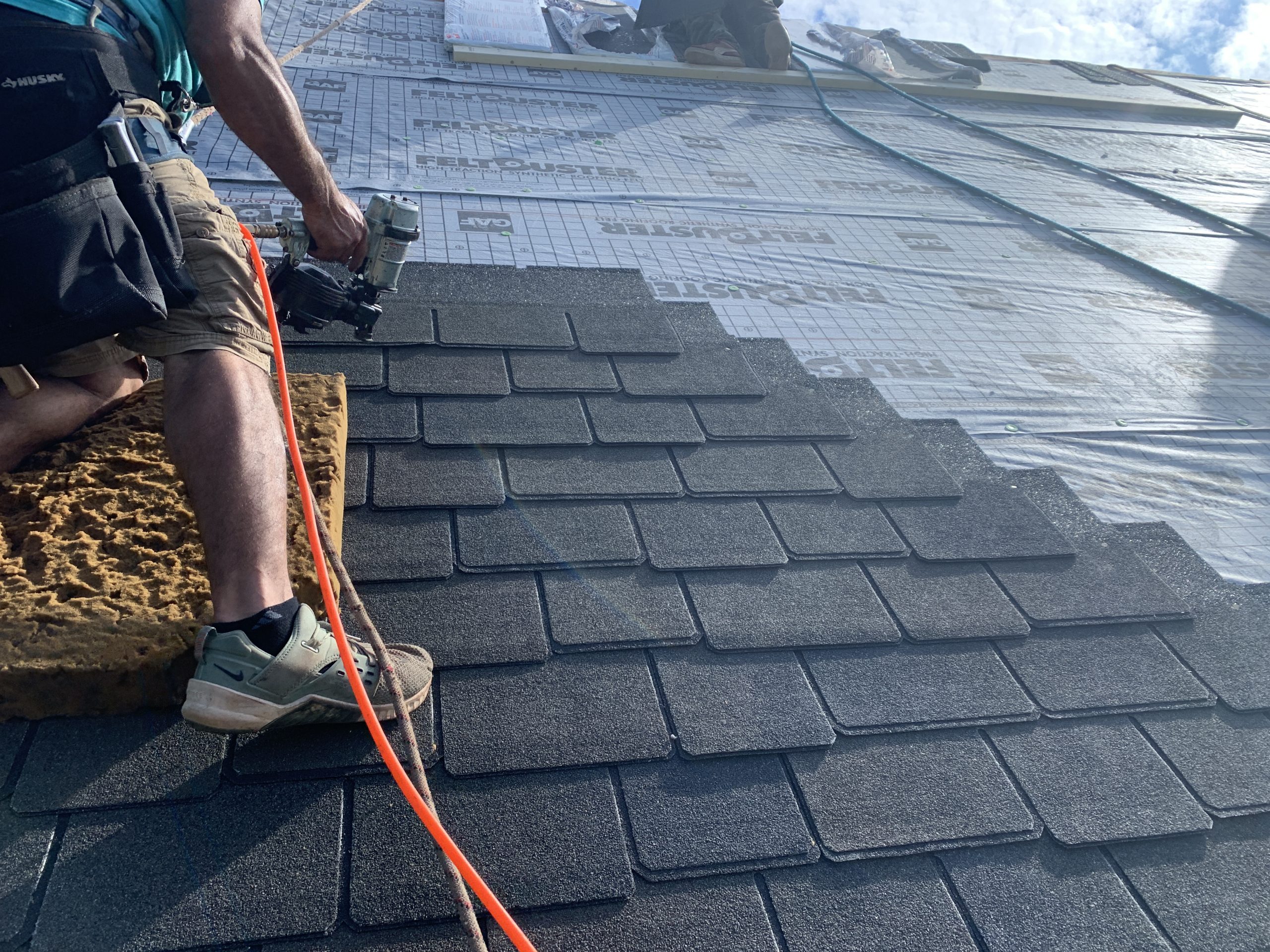 This is a view of shingles being installed. There is felt installed and shingles being nailed over the felt. 