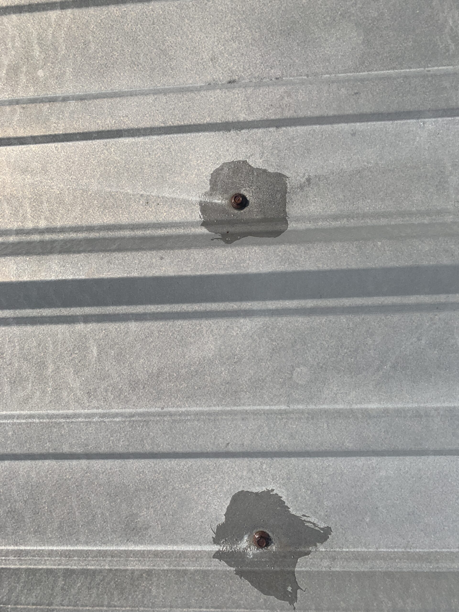 this is a picture of a grey metal roof and the roof screws that are in bad shape because they are rusting and causing leaks