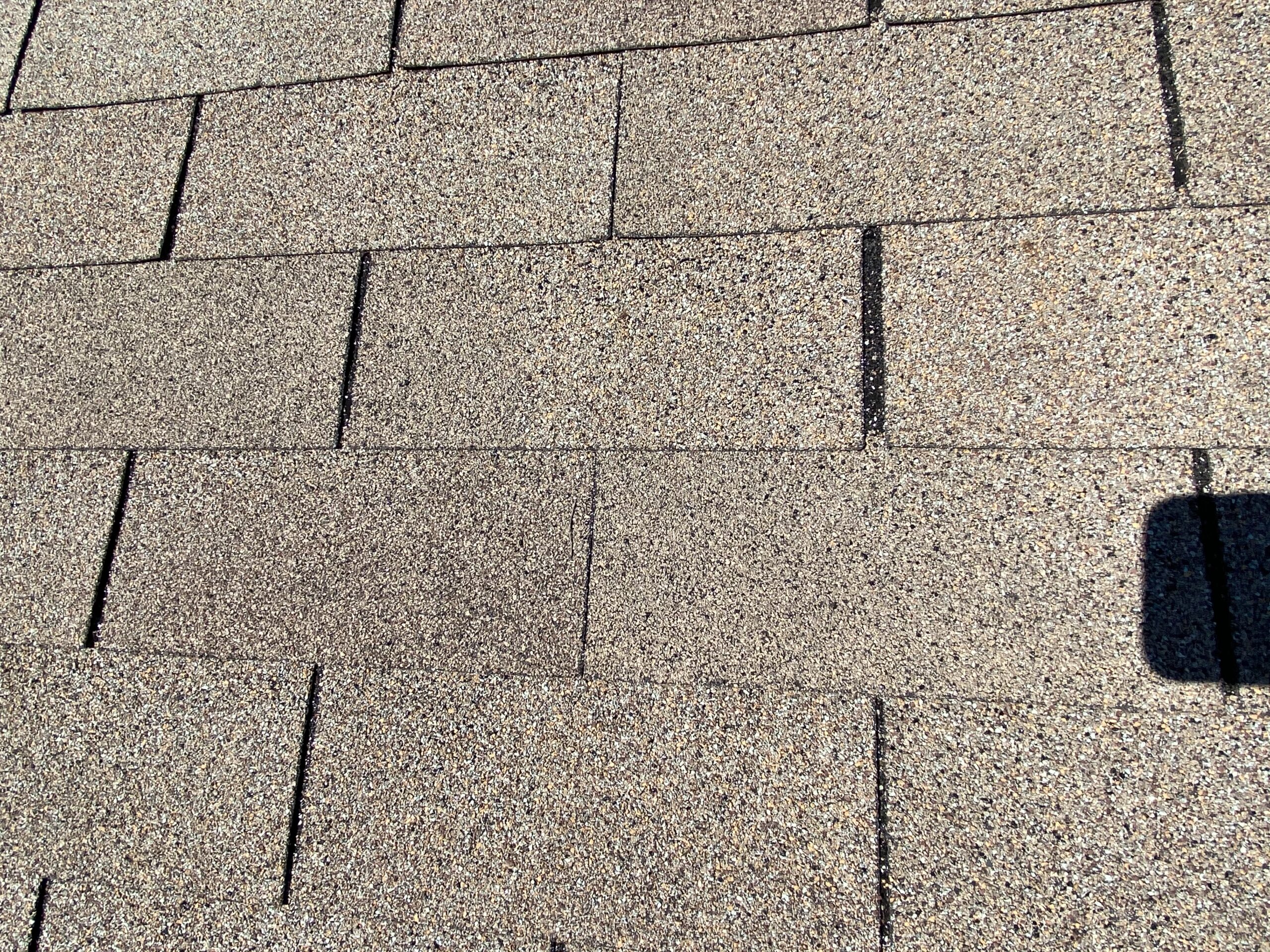 This is a picture of shingles that are misaligned on a gray colored roof