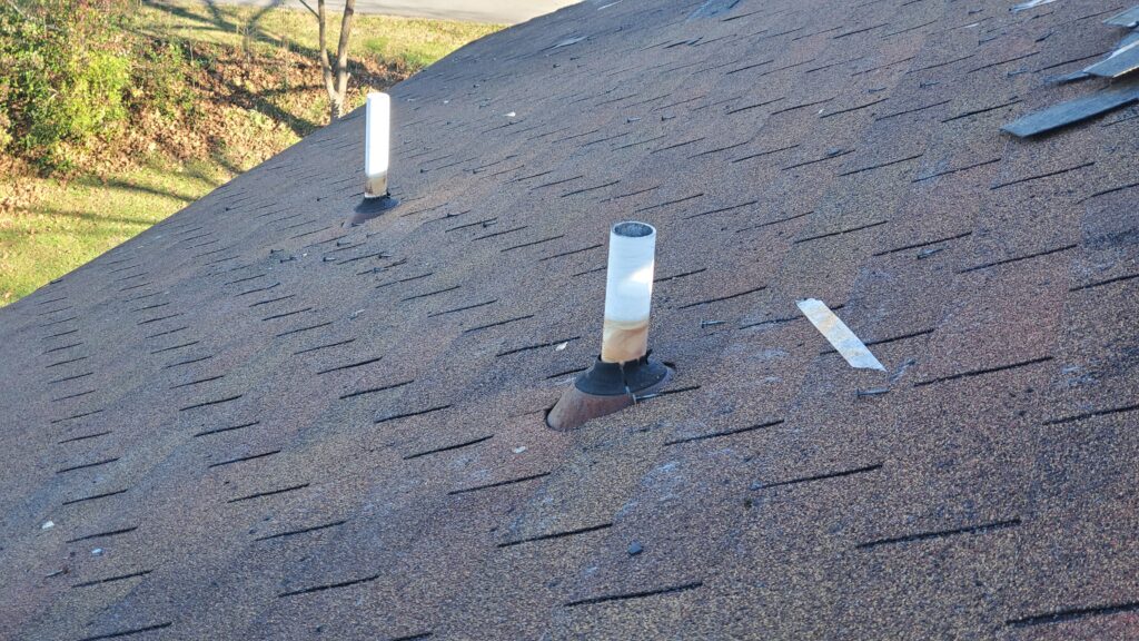 This is a picture of a roof from on top of the roof. There are whit pvc pipes sticking through the roof with pipe boots on them