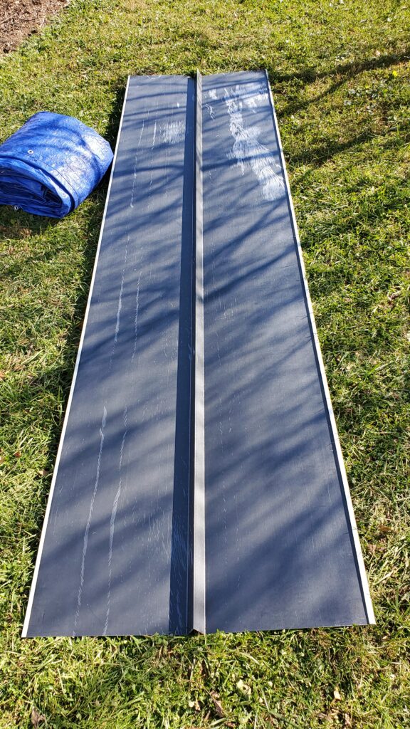 This is a picture of a grey piece of valley metal laying on a section of grass next to a folded up blue tarp