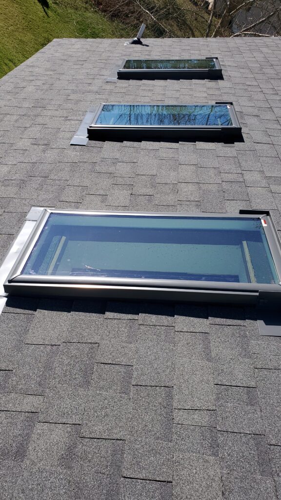 This is a picture of 3 new skylights that have just been installed on a new grey shingle roof