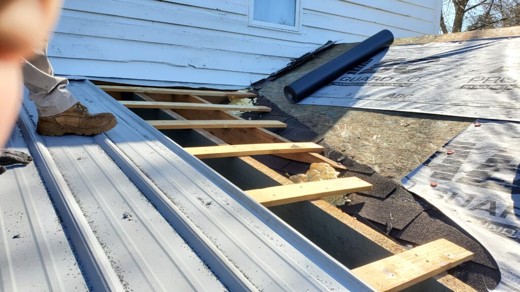 This is a picture of a metal roof that busts up against a wooden roof. The metal is on the left side of the picture and 3 of the metal panels are removed 