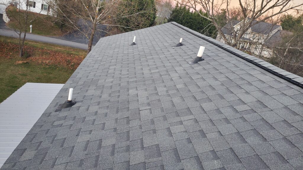 This is a picture of a grey shingle roof with 4 pipes with pipe boots on them sticking through the roof