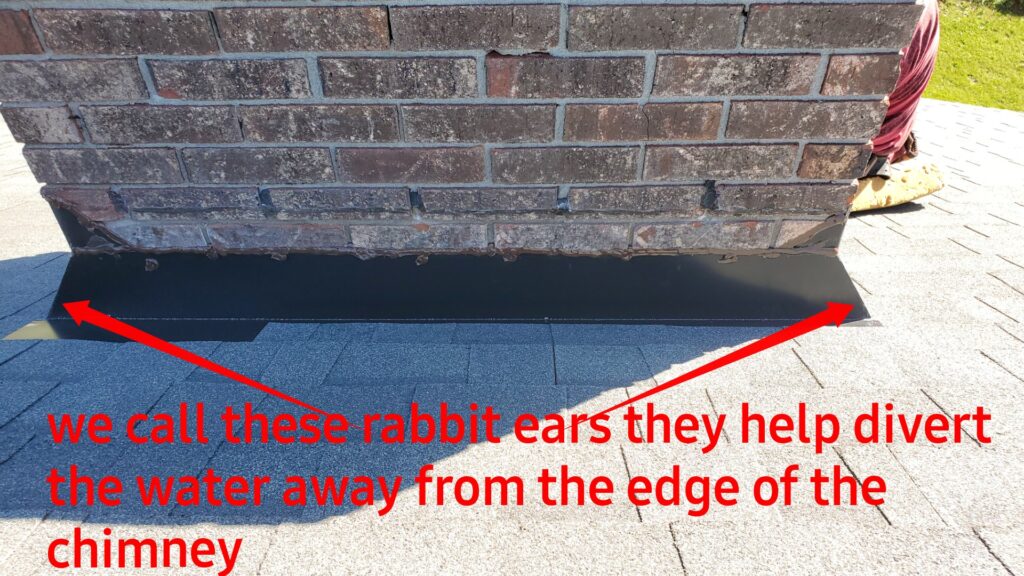 This is a picture of the back side of a chimney that has black metal around it. It also has red arrows pointing to the edge of the flashing