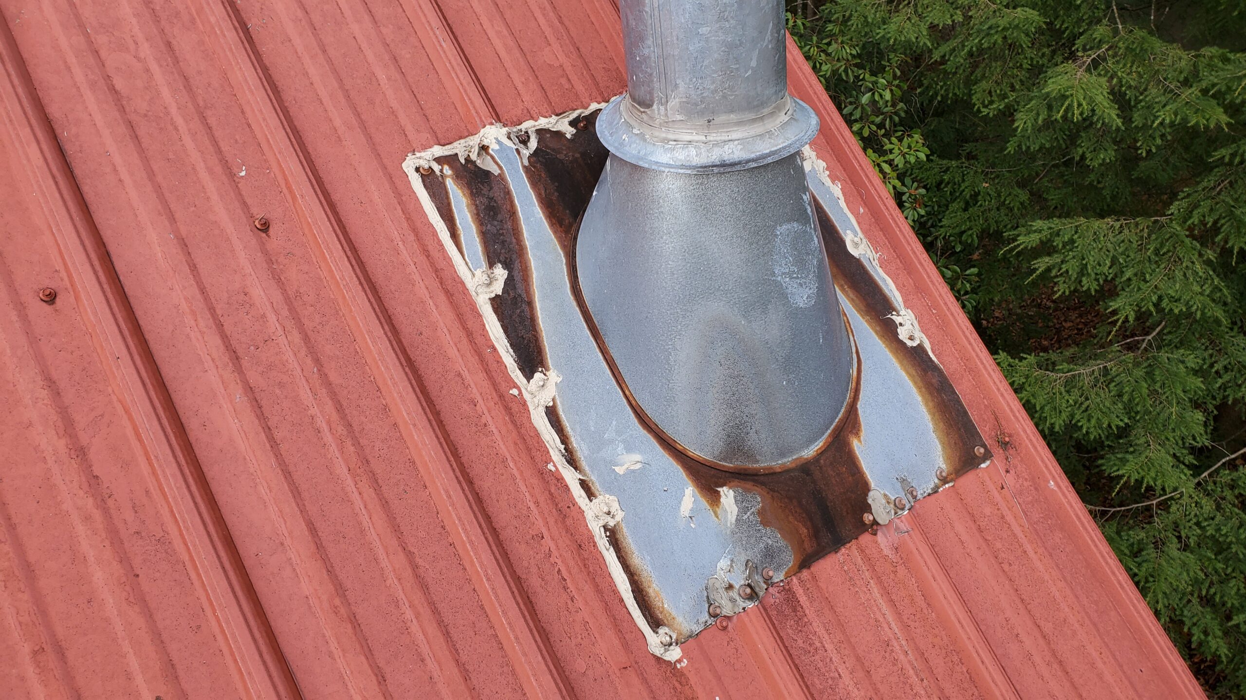 This is a picture of a metal chimney vent ontop of a red metal roof that is rusted and old