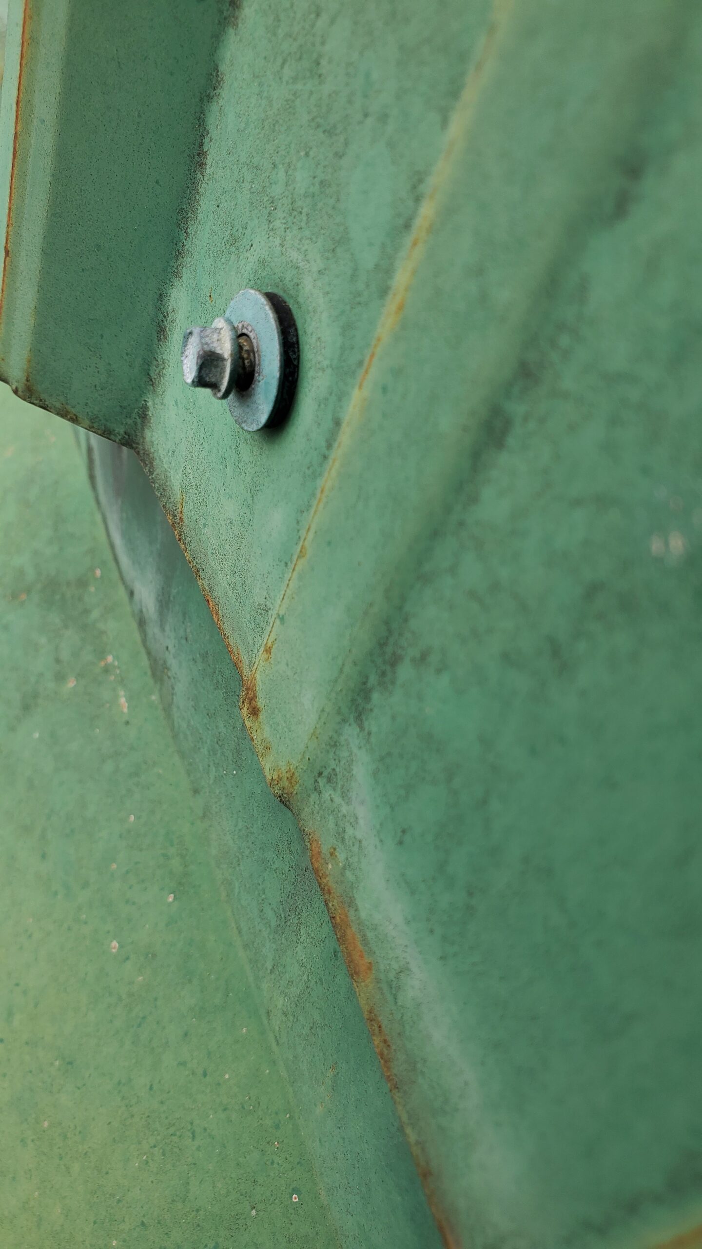 This is a up close picture of a green metal roof with a screw backing out of the metal roof