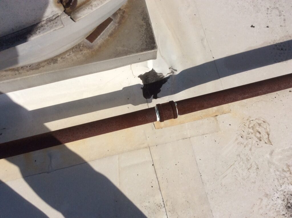 This is a view of a rusted pipe on a white commercial flat roof.