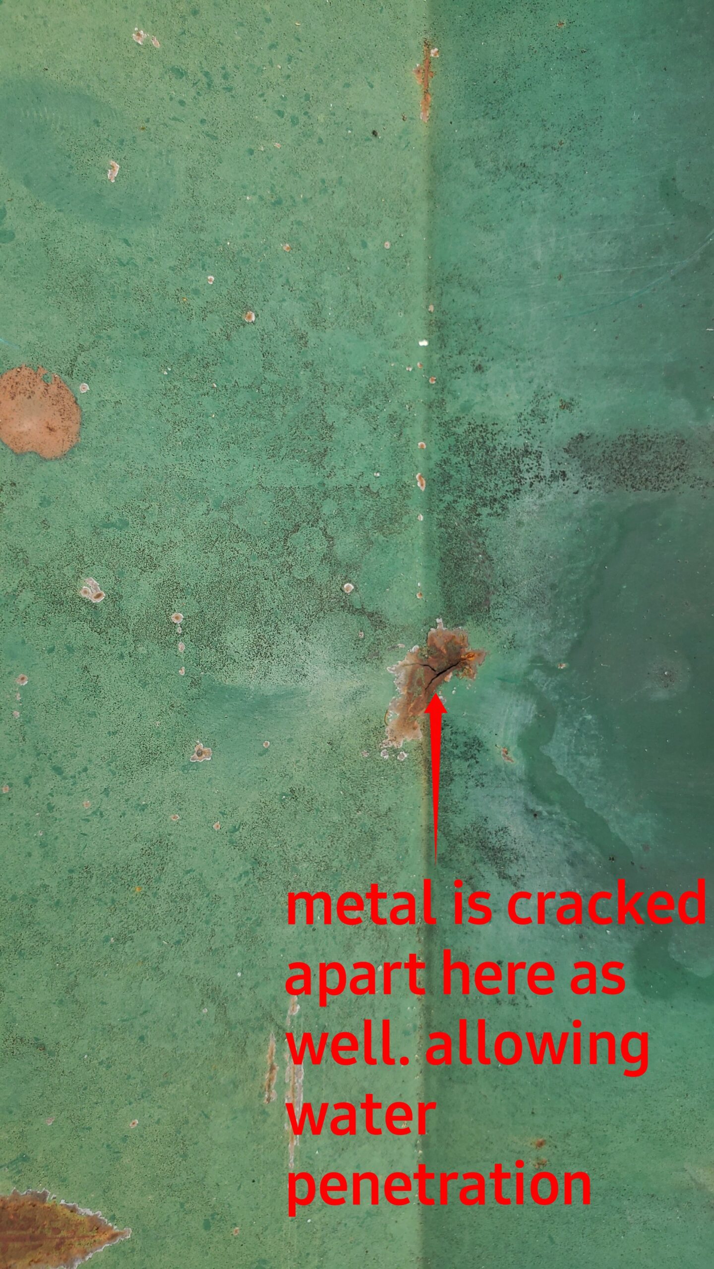 This is a picture of a green metal roof with a rusted spot that is cracked allowing water in