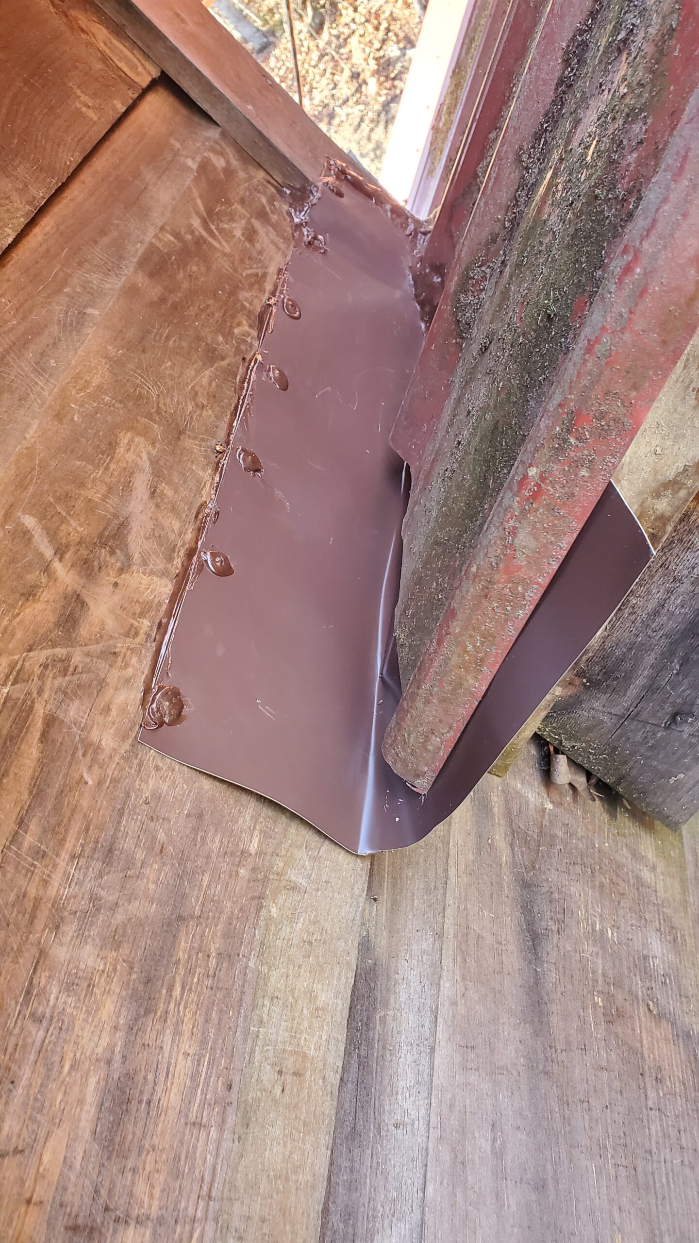  This is a picture of a red piece of metal flashing that goes under the metal roofing and butts up against a wooden wall and is sealed and screwed to the wall 