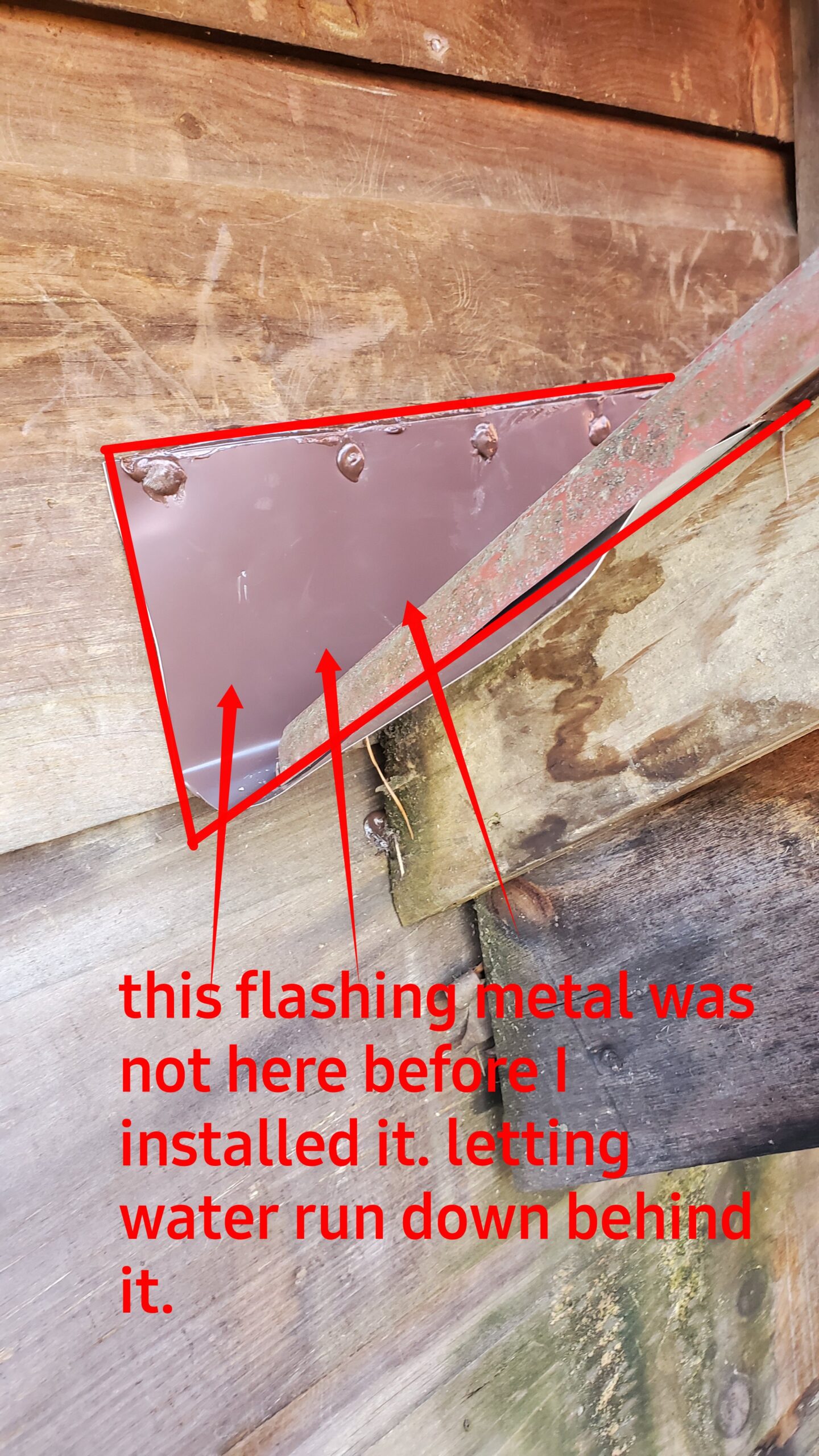 This is a picture of a red piece of metal flashing that goes under the metal roofing and butts up against a wooden wall and is sealed and screwed to the wall 