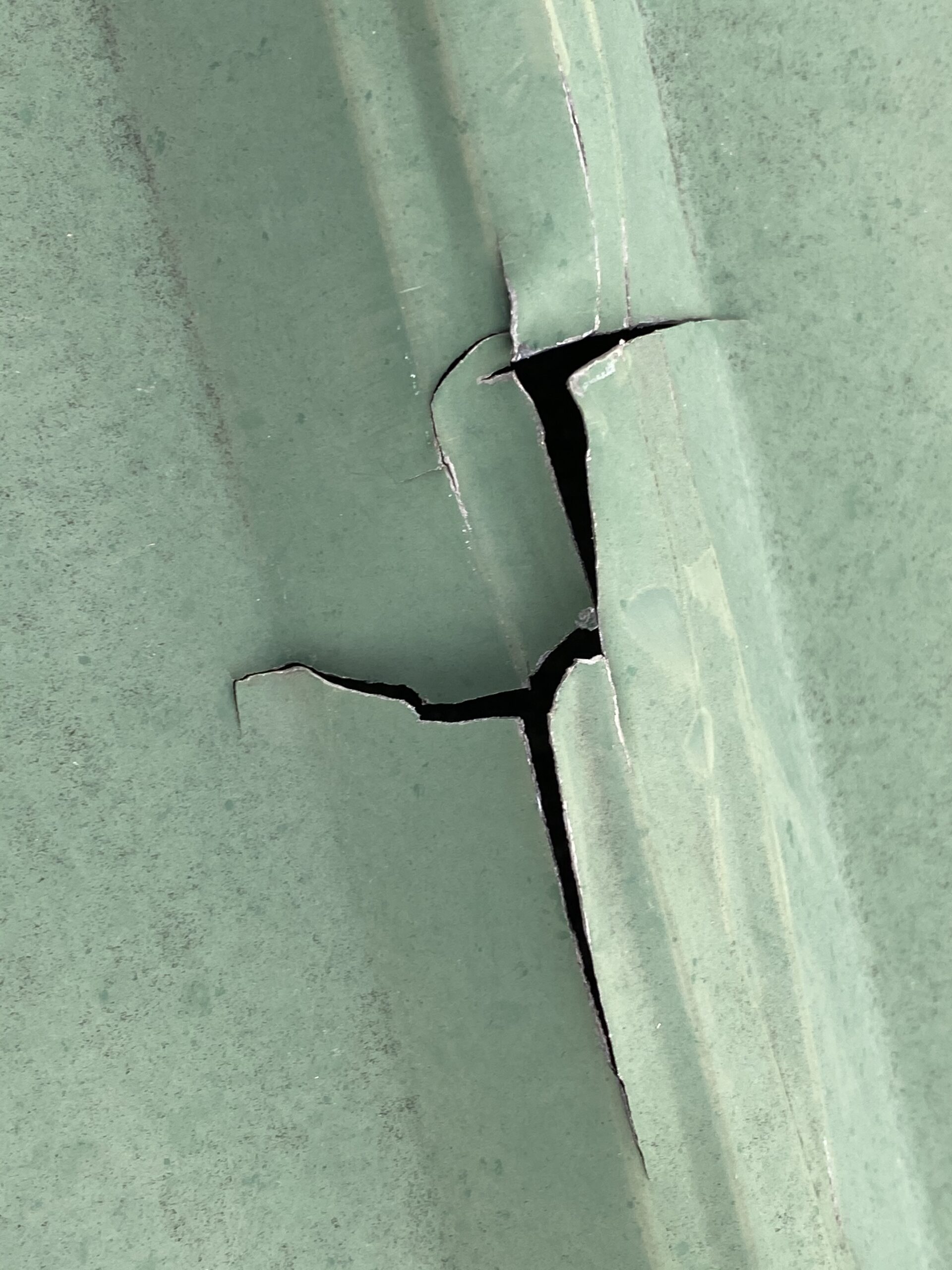 This is a view of a green metal roof panel with a large crack.