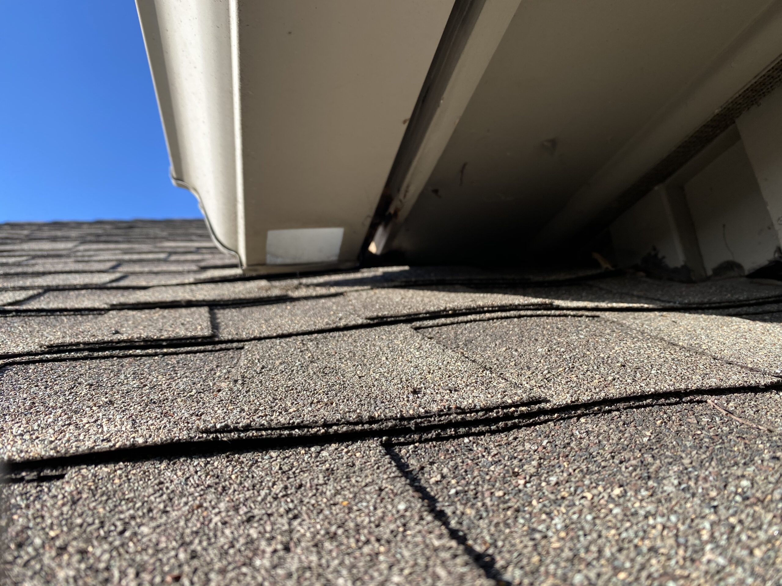 This is a picture of a wicker colored gutter with a hole in it and brow shingle roof.