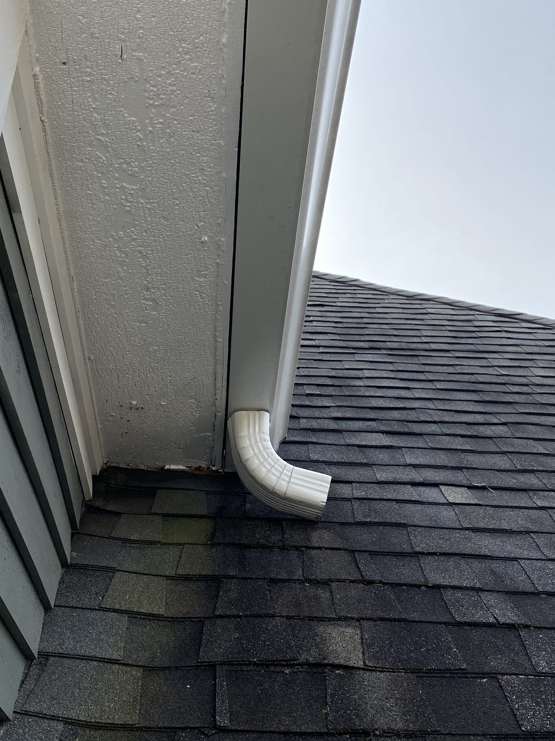 This is a picture of an elbow downspout that is pointing directly to the side of the shingle