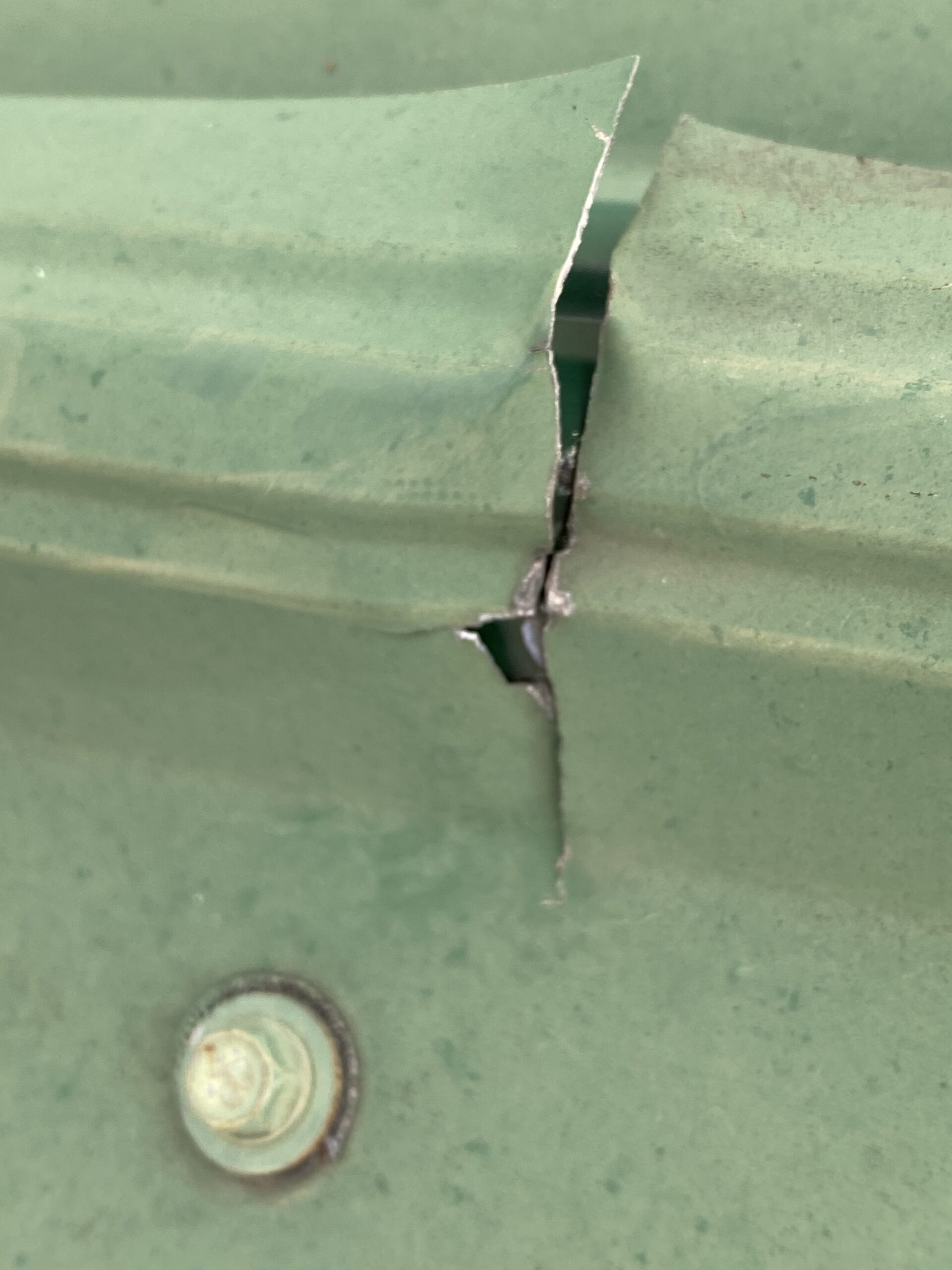 This is a view of a green metal roof panel with a crack in the metal. 