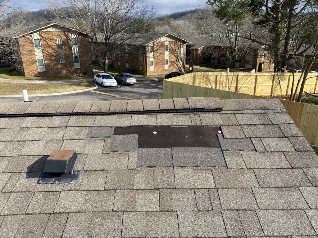 This is a picture of a brown roof that is missing about four shingles at the ridge.