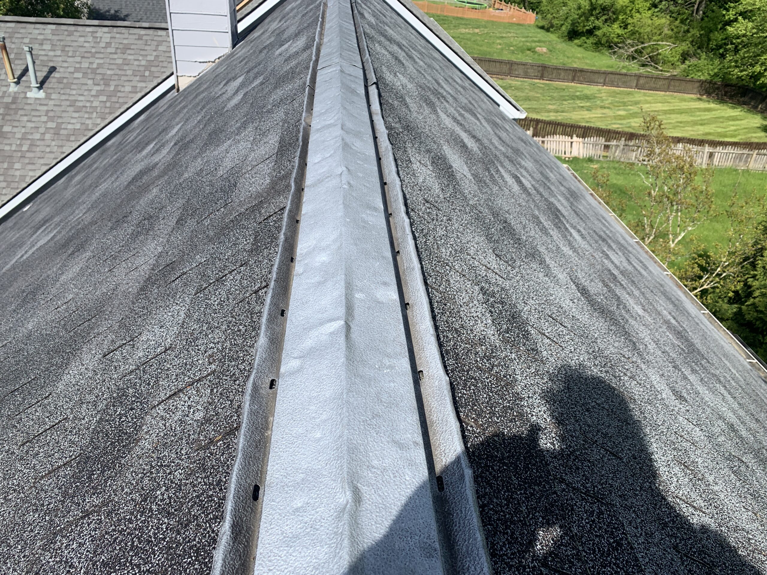 This image shows large dents and perforations on the metal ridge cap and shingles