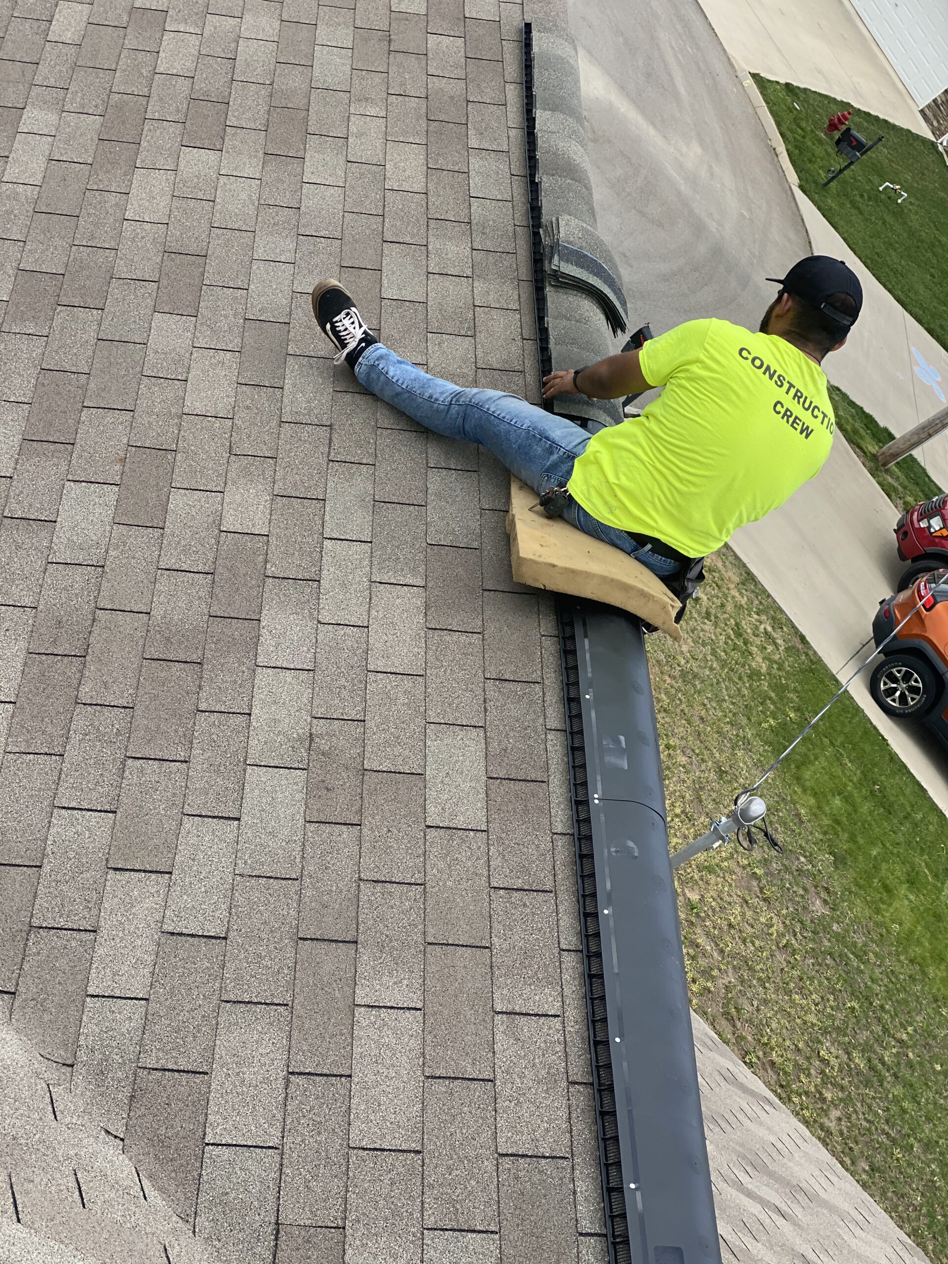 This is a picture of a person installing ridge cap shingles on a black ridge vent